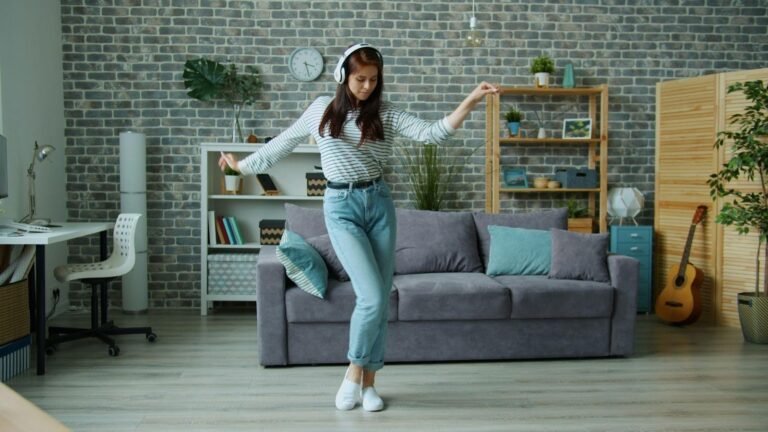 Woman wearing headphones dancing in a stylish living room with sofa, plants, and shelves in the background.
