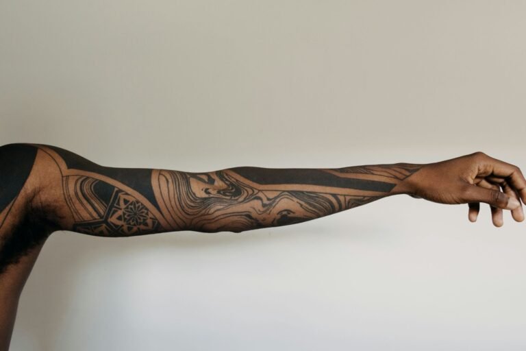 Extended arm showing a bold geometric blackwork sleeve tattoo with flowing abstract patterns.
